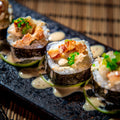 Sushi rolls with seafood and green vegetables on a black plate.